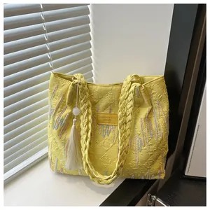 Dettaglio di borsa tote gialla con manici intrecciati e ricami a onde dai colori vivaci