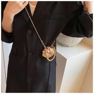 Dettaglio di una mini borsa a tracolla dorata a forma di conchiglia su una modella alla moda