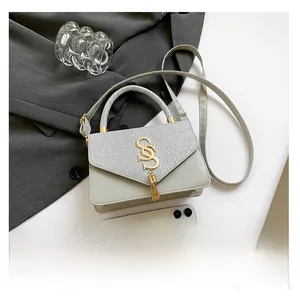 Detail of grey crossbody bag featuring a golden S-clasp and delicate tassel pendant
