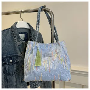 Dettaglio della borsa tote azzurra con ricami multicolore e ciondolo a nappa verde