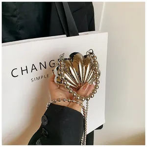 Dettaglio di una mini borsa creativa in metallo dorato a forma di conchiglia con catene