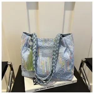 Dettaglio borsa tote azzurra trapuntata con ricami colorati e manici intrecciati