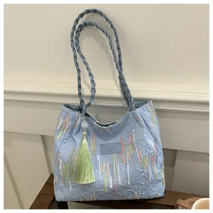 Dettaglio della borsa tote azzurra ricamata con manici intrecciati e nappa verde