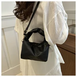 Detail of black pleated handle handbag with adjustable strap and gold metal hardware