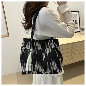 Dettaglio borsa tote nera con ricami colorati, tracolla intrecciata e nappa bianca