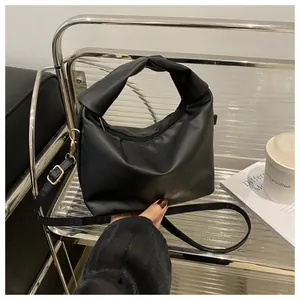Detail of a black crossbody bag featuring a unique knotted handle and matte leather finish