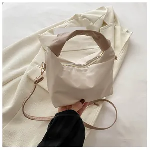 Detail of off-white pleated handbag featuring a twisted brown handle and metal zipper