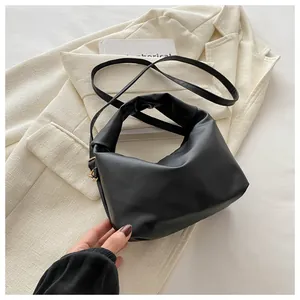 Detail of black pleated cloud bag with soft handle and golden hardware on beige blazer