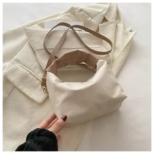 Detail of minimalist cream pleated bag featuring dark brown handles and golden metal buckles