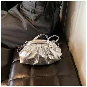 Detailed view of silver metallic pleated cloud bag on dark leather surface