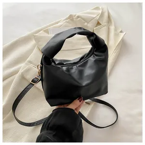Detail of black crossbody bag with pleated texture, knot handle and gold hardware
