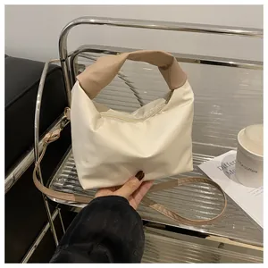 Detail of minimalist cream square bag with twisted khaki handle and adjustable strap