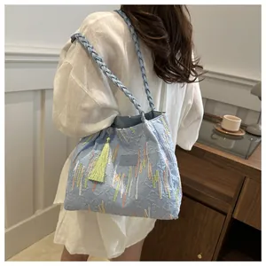Dettaglio del tessuto blu strutturato con ricami colorati e nappa verde sulla borsa