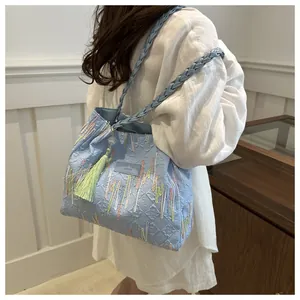 Dettaglio borsa ricamata azzurra con tracolle intrecciate e nappa di velluto verde scuro