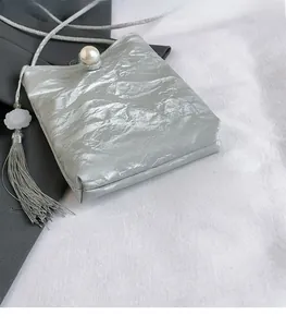Detail of silver metallic wrinkled bag with large pearl clasp and floral tassel charm