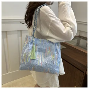 Dettaglio borsa tote trapuntata azzurra con ricami colorati e nappa decorativa verde