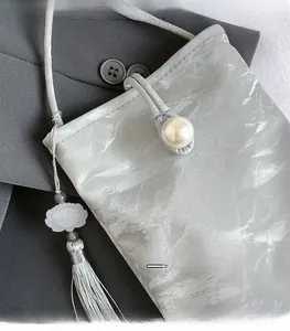 Detail of light gray textured phone bag featuring a pearl clasp and lotus tassel charm