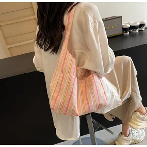 Detail view of pink and yellow vertical striped canvas tote bag worn by a model in a cafe