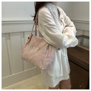 Dettaglio della borsa rosa con ricamo e tracolla intrecciata indossata da una modella