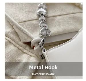 Detail of silver heart-shaped chain and polished hardware hook on white leather handbag