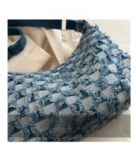 Detail of blue denim tote bag featuring distressed fringe checkerboard texture and fabric strap
