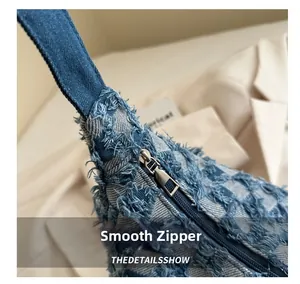 Close-up of smooth silver zipper and frayed denim texture on crescent handbag