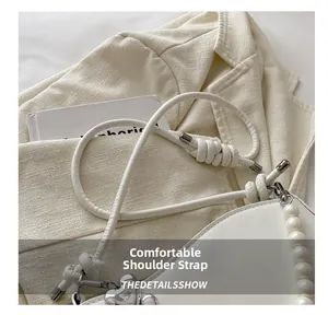 Detail of white shoulder strap with knot, pearl charm and silver heart on handbags