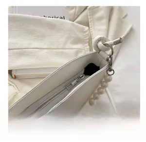 Close-up of cream white handbag featuring smooth zipper and elegant pearl strap detail