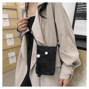 Detail of black pleated crossbody bag with white pearl buckle and tassel on beige coat