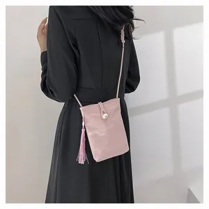 Detail of pink pleated crossbody phone bag with pearl buckle and tassel on black dress