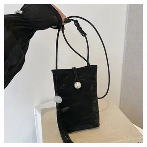 Detailed close-up of a black textured crossbody bag with a large pearl buckle and long tassels