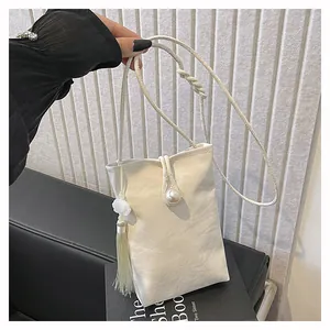Detail of white textured crossbody phone bag with elegant pearl clasp and long tassel