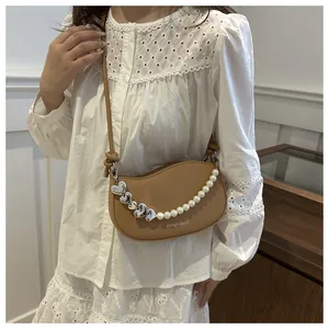 Detail of khaki half-moon bag with elegant pearl and silver heart chain decoration