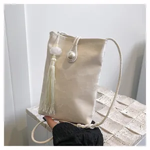 Detail of cream crossbody phone bag featuring pleated texture, pearl button and tassel
