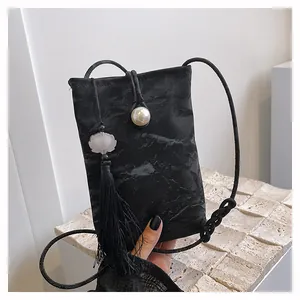Detail of black mini crossbody phone bag with pearl button closure and silk tassel