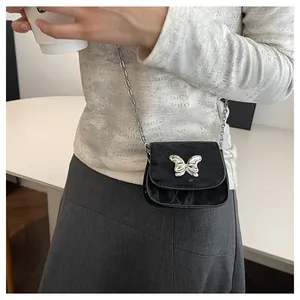 Detail of mini black saddle bag with silver butterfly buckle and metallic chain strap