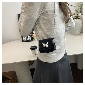 Close-up of black quilted mini crossbody bag with silver butterfly buckle on a model