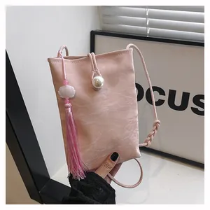 Detailed close-up of pink crossbody phone bag featuring large pearl clasp and long tassels