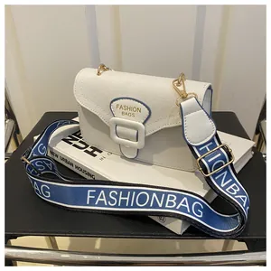 Detail der weißen Canvas-Umhängetasche mit blauem Logo-Schild und breitem Modegurt