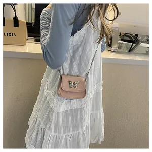 Pink mini crossbody bag with silver butterfly and metal chain worn over white dress
