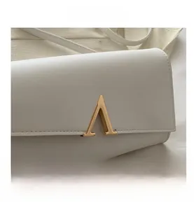 Gros plan du sac bandoulière minimaliste en cuir blanc avec logo décoratif en métal doré