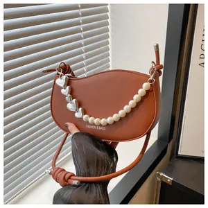 Detail of a brown leather half-moon bag featuring a pearl and metal heart charm chain
