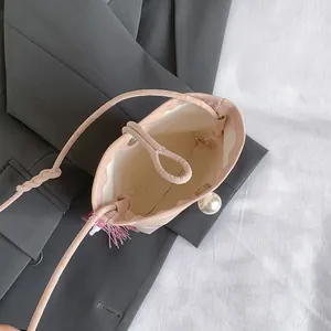 Pink drawstring mini bucket bag with tassel and pearl detail on grey suit background