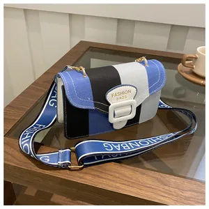 Detail der Farblock-Tasche mit blauem Stoffgurt auf einem Holz Tisch Arrangement