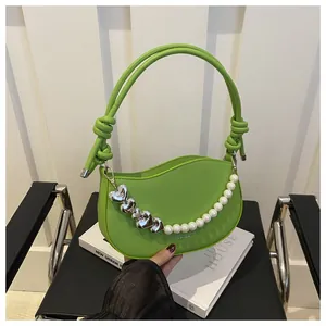 Detail of green crescent handbag featuring a decorative heart and pearl chain on a chair
