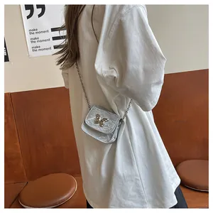 Detail of silver pleated mini saddle bag with golden butterfly and metal chain strap