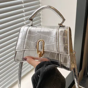 Detail of silver crocodile embossed mini handbag featuring a gold oval clasp and handle