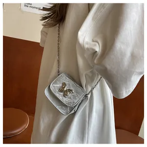 Detail of silver textured mini saddle bag featuring a gold butterfly buckle and chain