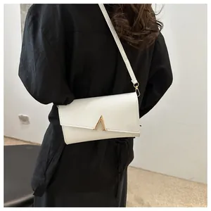 Détail d'un sac à bandoulière enveloppe blanc avec une boucle métallique dorée en forme de A