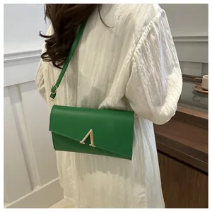 Sac à bandoulière vert rectangulaire avec boucle en V dorée porté par un mannequin